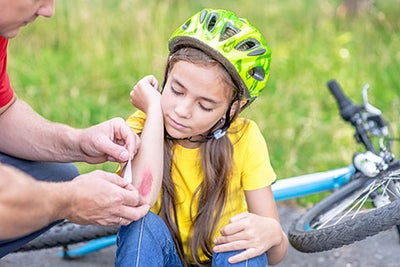 Dad puts a bandage on a wound to little girl, who fell off his bicycle