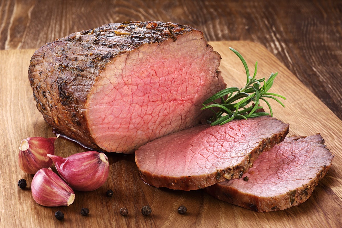 Baked meat, garlic and rosemary on a wooden background. Roast beef.