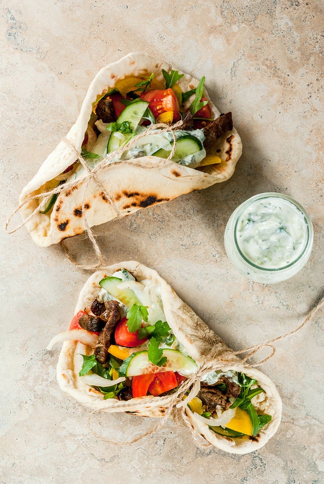 Healthy snack, lunch. Traditional Greek wrapped sandwich gyros - tortillas, bread pita with a filling of vegetables, beef meat and sauce tzatziki. On light stone table Copy space top view