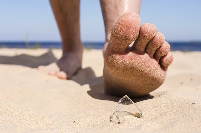 Man goes on the beach and the risk of stepping on a splinter of broken bottle glass, which is lying on the sand littered in places with poor environmental conditions